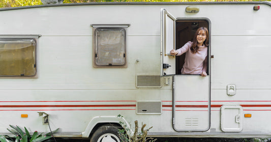 A happy young woman standing inside an RV camper opens the top window section of the door as she looks outside.